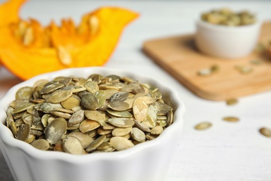 Photo of Bowl of raw pumpkin seeds on white table, closeup. Space for text