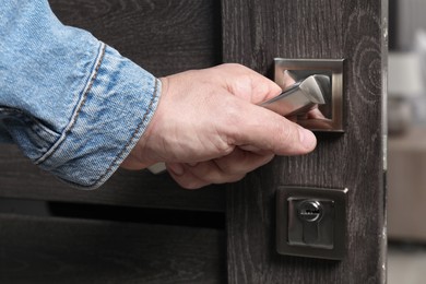 Man opening wooden door indoors, closeup of hand on handle