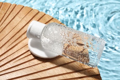 Wet bottle of micellar water and cotton pad on wooden board, closeup