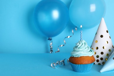 Delicious birthday cupcake with candle near party hats and balloons on light blue background, space for text