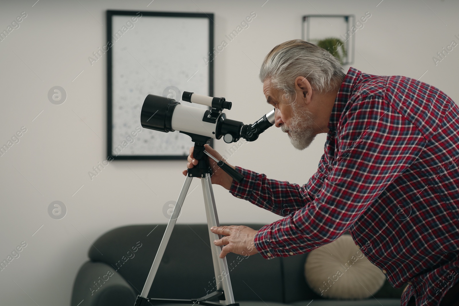 Photo of Senior man looking at stars through telescope in room