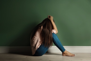 Photo of Depressed young woman on floor near color wall