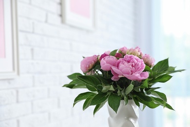 Photo of Vase with bouquet of beautiful peonies at white wall in room, space for text