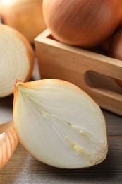 Whole and cut onions on wooden table, closeup