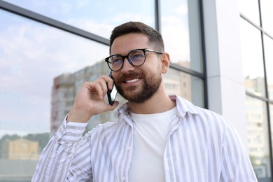 Photo of Handsome bearded man in glasses talking on phone outdoors