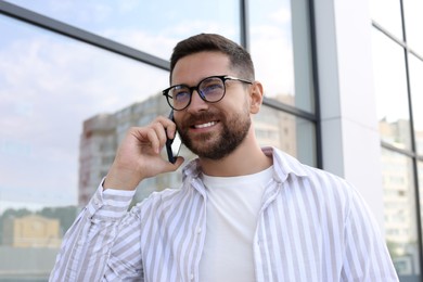 Handsome bearded man in glasses talking on phone outdoors