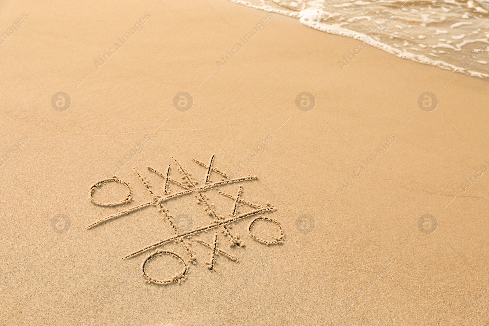 Photo of Tic tac toe game drawn on sand near sea, space for text