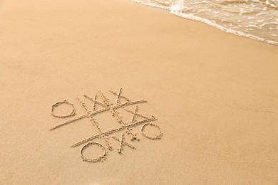 Tic tac toe game drawn on sand near sea, space for text