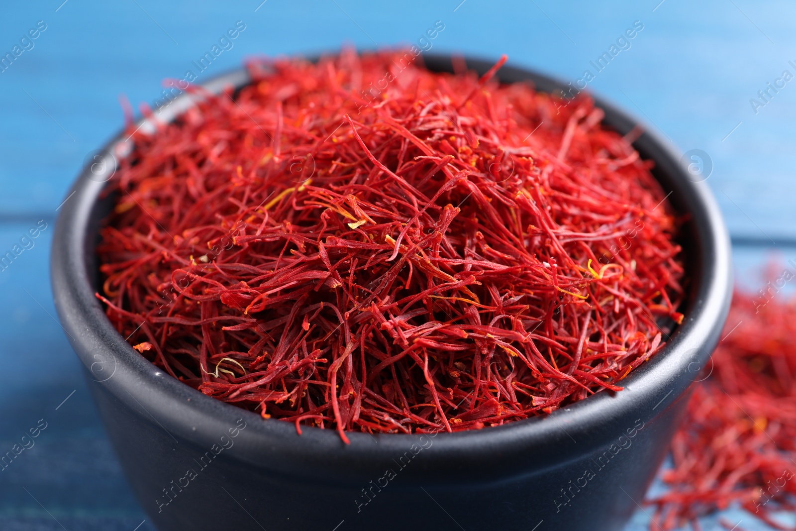 Photo of Dried saffron in bowl on blue table, closeup