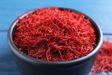 Photo of Dried saffron in bowl on blue table, closeup
