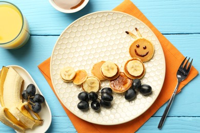 Creative serving for kids. Plate with cute caterpillar made of pancakes, grapes and banana on light blue wooden table, flat lay