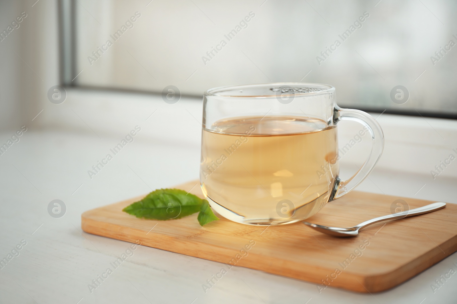 Photo of Tasty hot green tea in cup on window sill, closeup