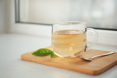 Photo of Tasty hot green tea in cup on window sill, closeup