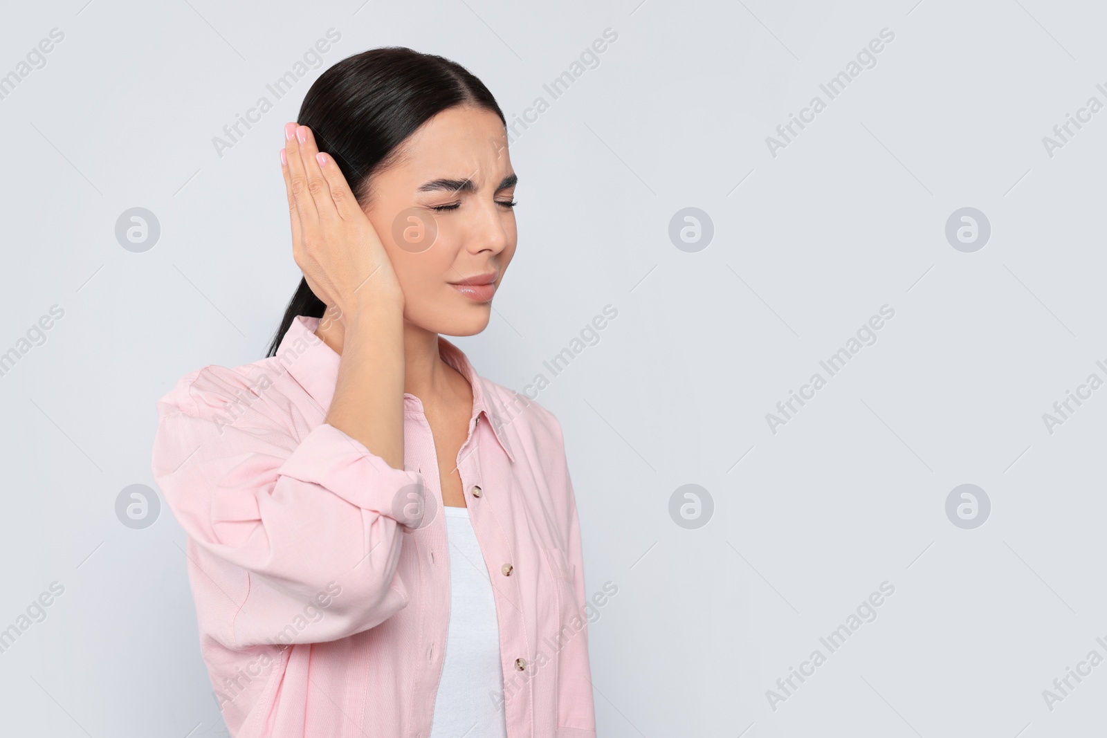 Photo of Young woman suffering from ear pain on light grey background. Space for text