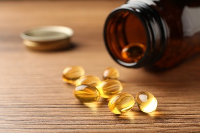 Overturned bottle with dietary supplement capsules on wooden table, closeup