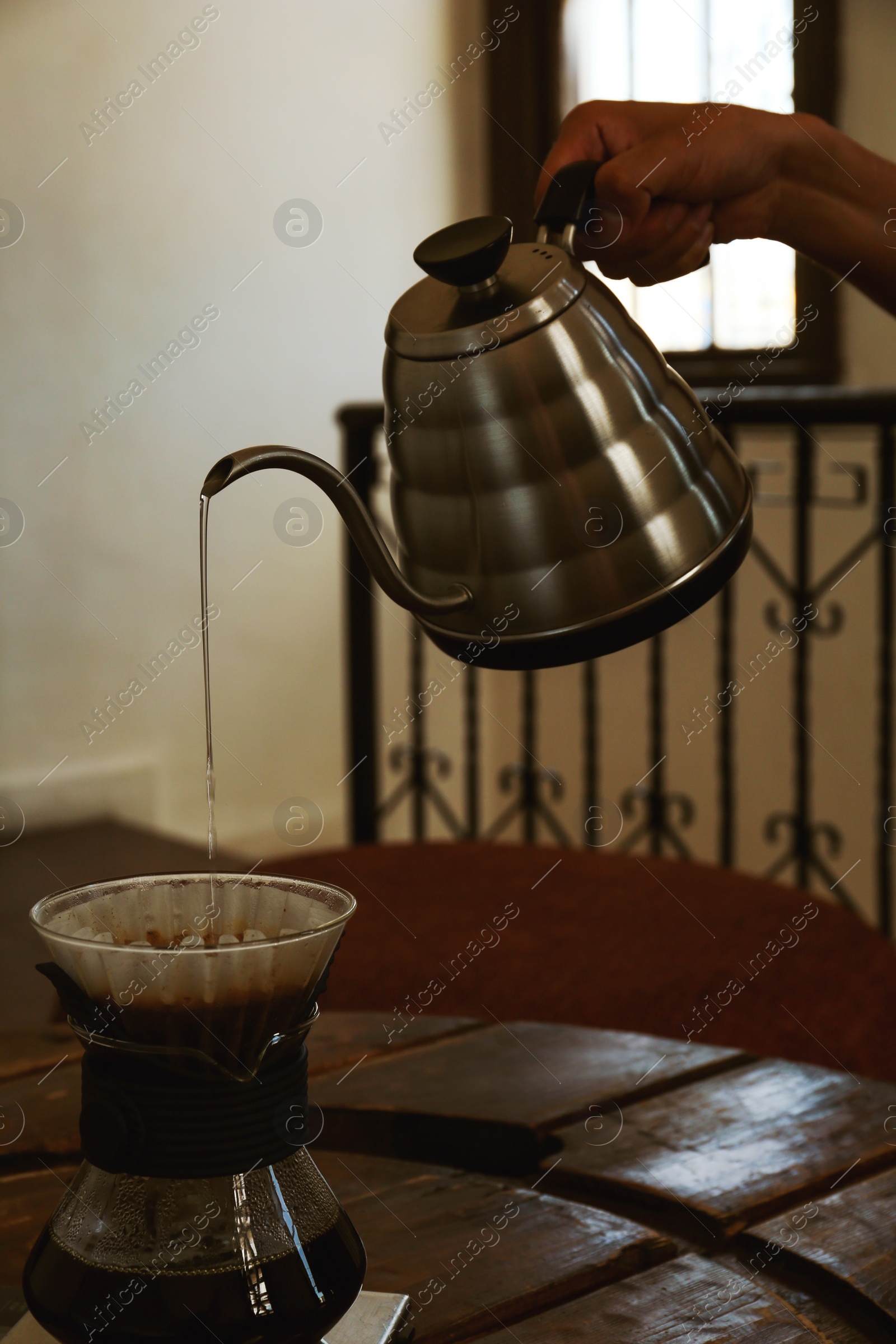Photo of Barista pouring water from kettle into cup with coffee and wave dripper in cafe, closeup