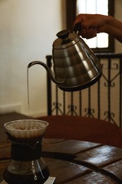 Barista pouring water from kettle into cup with coffee and wave dripper in cafe, closeup
