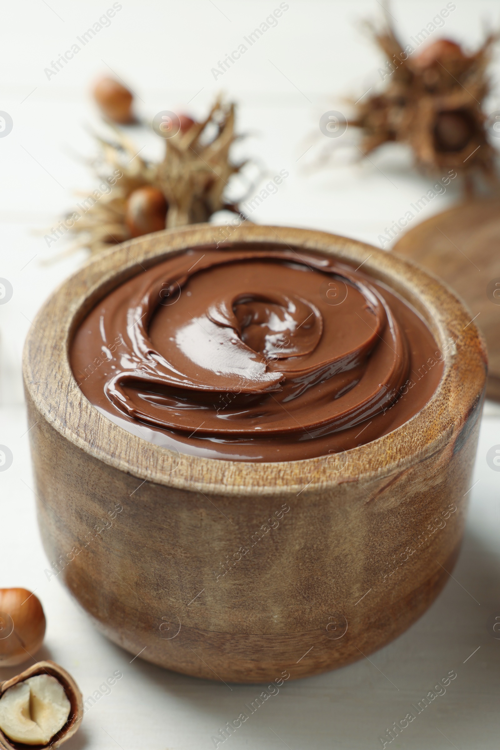 Photo of Bowl of tasty chocolate paste with hazelnuts on white wooden table