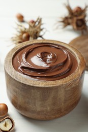 Photo of Bowl of tasty chocolate paste with hazelnuts on white wooden table
