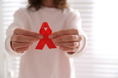 Photo of Woman holding red awareness ribbon on light background, closeup. World AIDS disease day