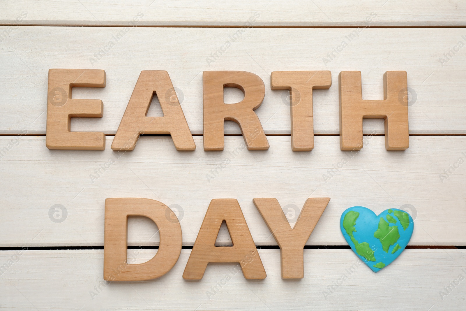 Photo of Words Earth Day and heart shaped plasticine planet on white wooden table, flat lay
