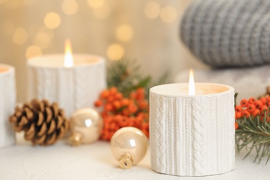 Holders with burning candles and decoration on white table against blurred Christmas lights