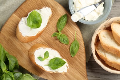 Photo of Delicious sandwiches with cream cheese and basil leaves on wooden table, flat lay