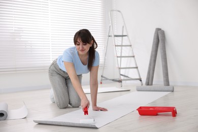 Photo of Woman applying glue onto wallpaper sheet in room