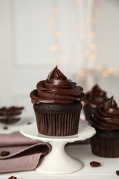 Dessert stand with delicious chocolate cupcake on white table against blurred lights. Space for text