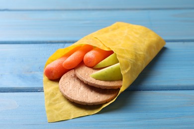 Photo of Different products in beeswax food wrap on light blue wooden table, closeup