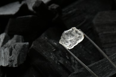 Tweezers with shiny rough diamond over coal, closeup. Space for text