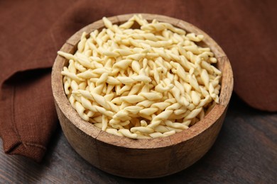 Uncooked trofie pasta in bowl on wooden table, closeup