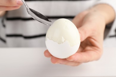 Photo of Woman eating boiled egg with spoon at white table, closeup