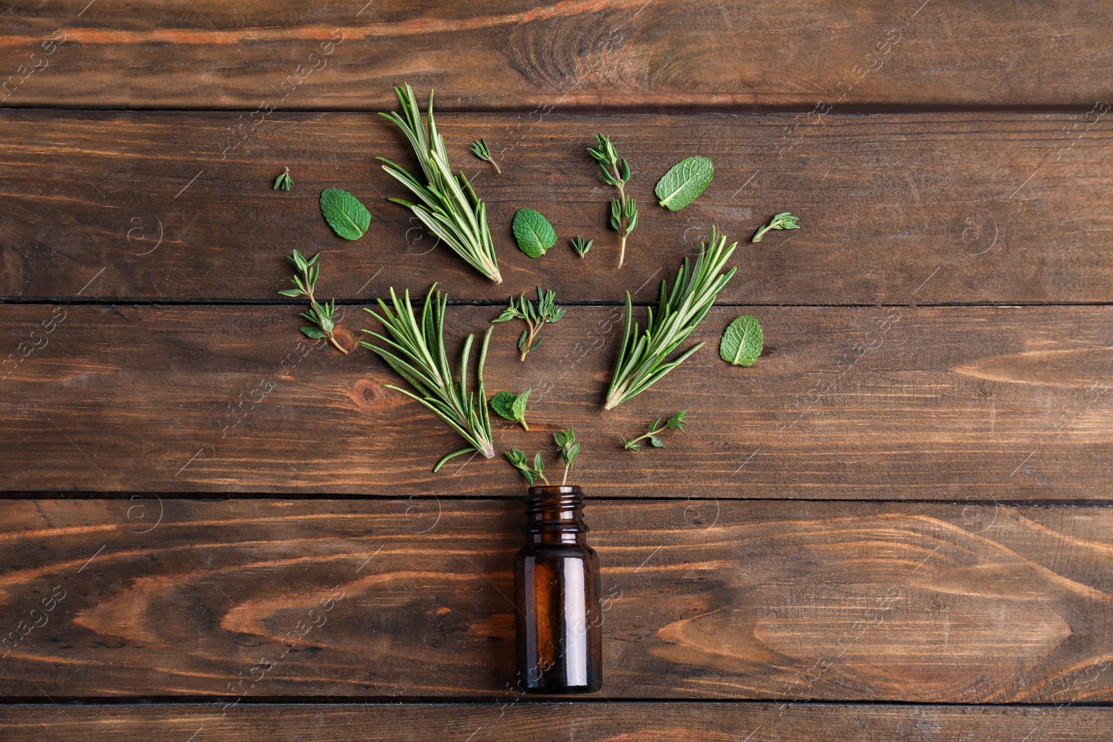 Photo of Bottle with essential oil and fresh herbs on wooden background, flat lay