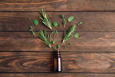 Bottle with essential oil and fresh herbs on wooden background, flat lay