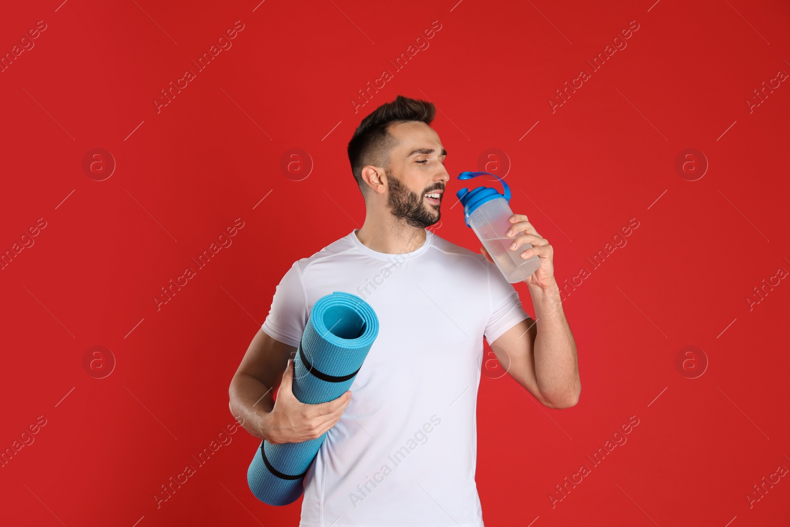 Photo of Handsome man with yoga mat drinking water on red background