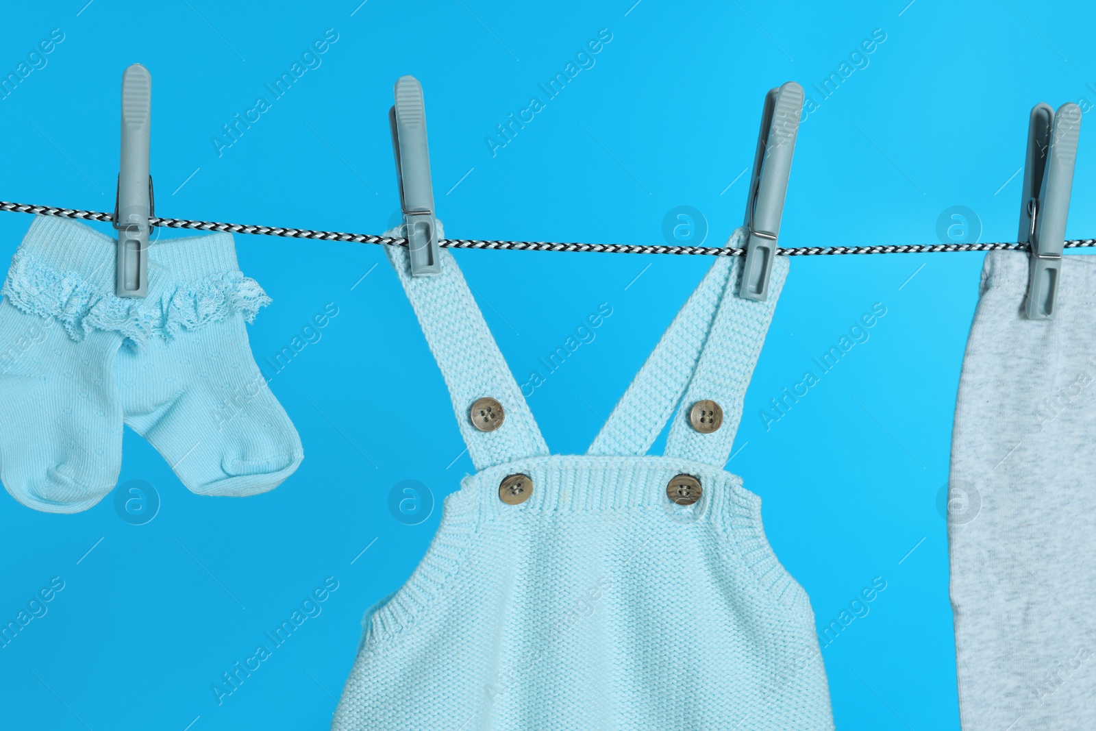 Photo of Different baby clothes drying on laundry line against light blue background, closeup