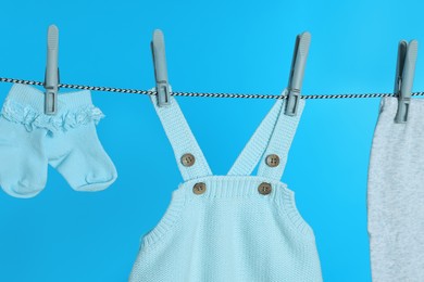 Photo of Different baby clothes drying on laundry line against light blue background, closeup