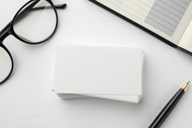 Photo of Blank business cards, glasses, notebook and pen on white table, flat lay. Mockup for design