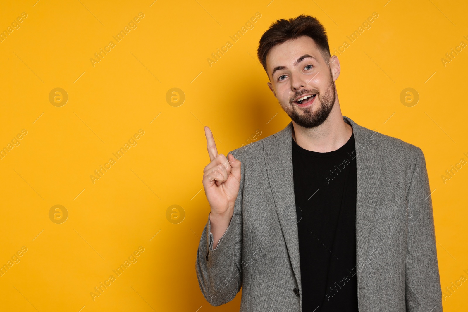 Photo of Handsome man in stylish grey jacket pointing at something on yellow background, space for text