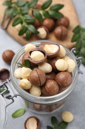 Photo of Tasty Macadamia nuts in jar on light grey table, closeup