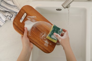 Photo of Woman washing wooden cutting board at sink in kitchen, top view
