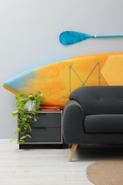 Photo of SUP board, paddle and stylish sofa in living room. Interior design