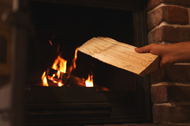 Photo of Man putting dry firewood into fireplace at home, closeup. Winter vacation