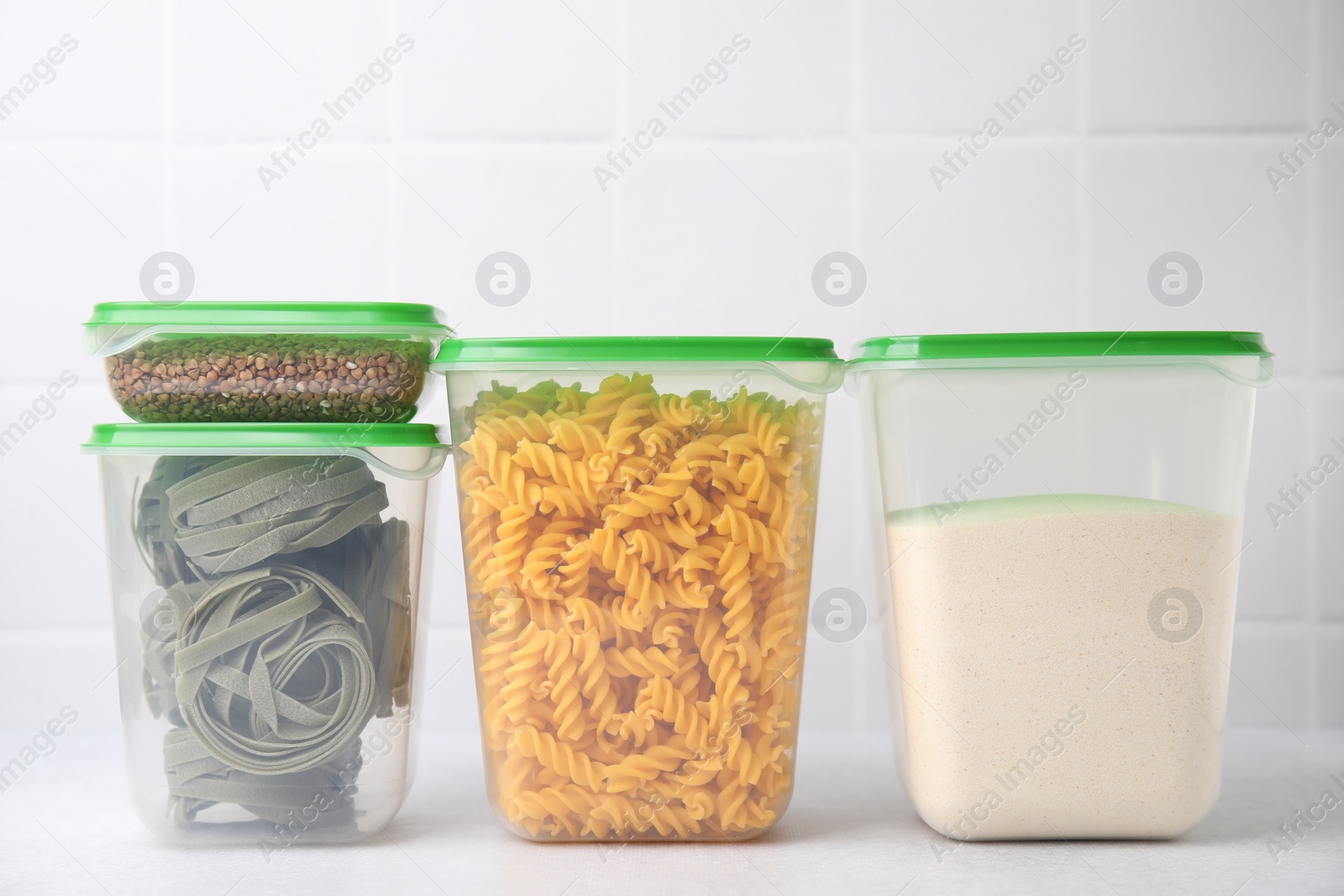 Photo of Plastic containers filled with food products on white table near tiled wall