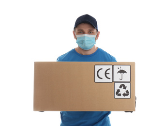 Photo of Courier in mask holding cardboard box with different packaging symbols on white background. Parcel delivery