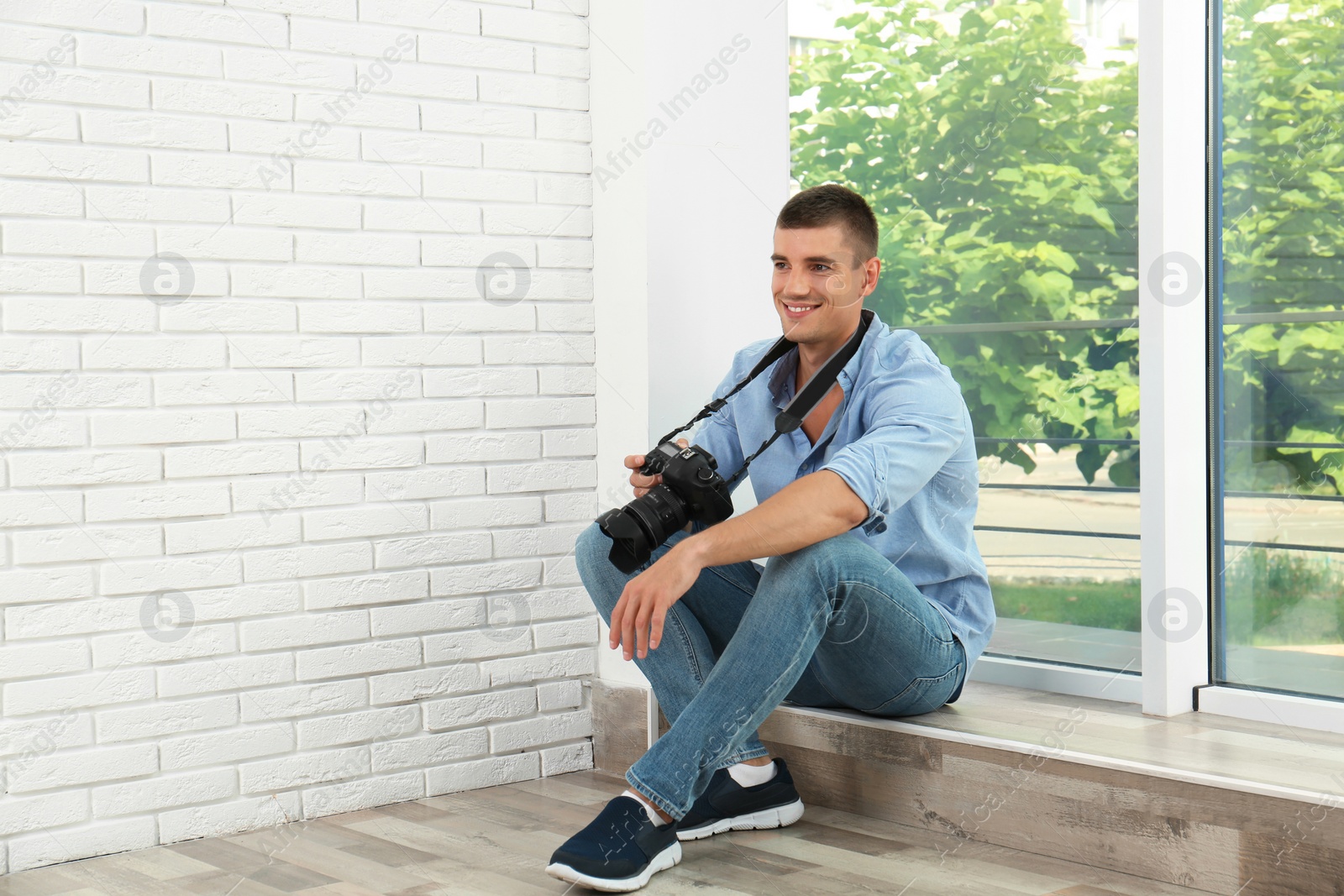 Photo of Young photographer with professional camera near window indoors. Space for text