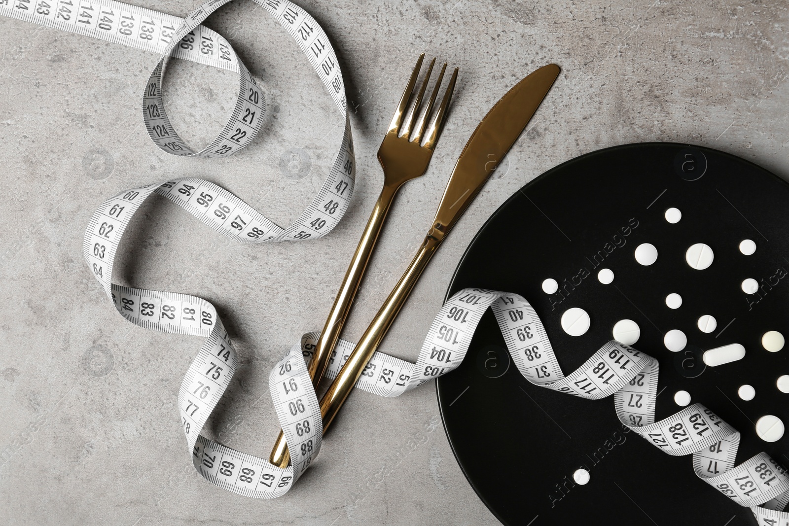 Photo of Plate with weight loss pills, cutlery and measuring tape on gray background, flat lay