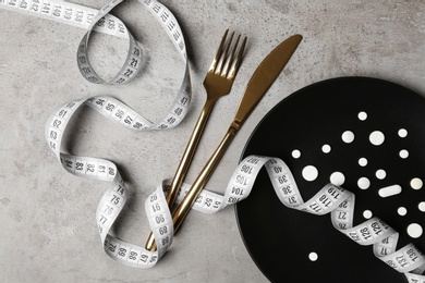 Plate with weight loss pills, cutlery and measuring tape on gray background, flat lay