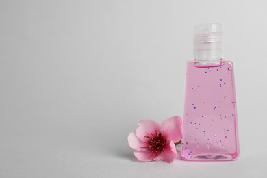 Photo of Bottle with antiseptic gel and flower on light grey background, space for text